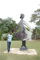 Dominic Benhura next to one of his works at his outdoor sculpture studio