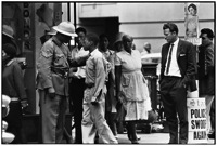 During a “swoop,” police are everywhere, checking passes. Young boy is stopped for his pass as white plainclothesman looks on. Checks go on in the townships, too.